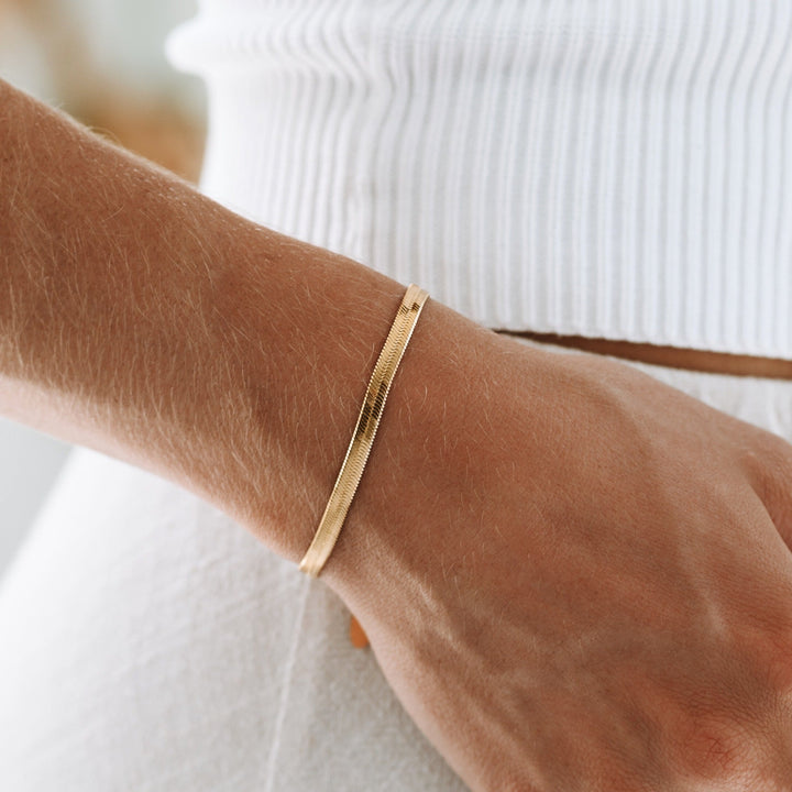 Close-up of elegant women's gold herringbone chain bracelet, perfect for layering.