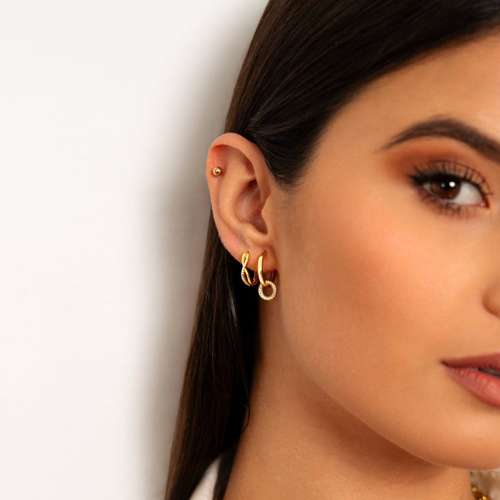 Close-up of women's sparkling gold crossed zirconia earrings, beautiful elegant jewelry.