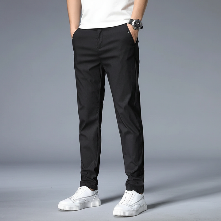 Model wearing comfortable men's elastic slim fit trousers in a casual office setting, side view.