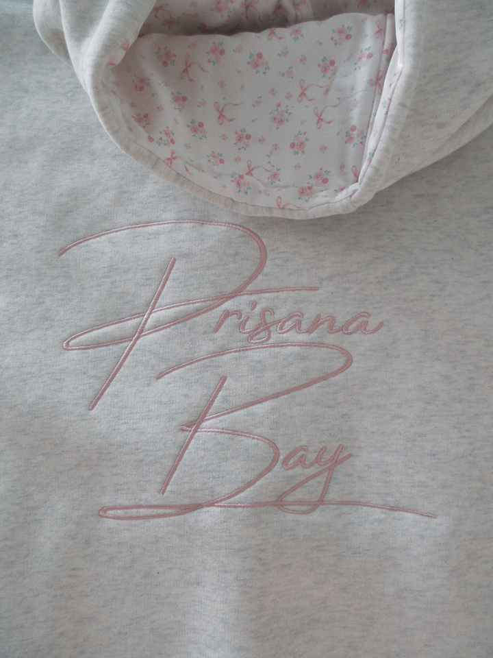 White Elodie women's hoodie, relaxed fit, soft fabric, with a charming pink bow detail. Casual & cozy.