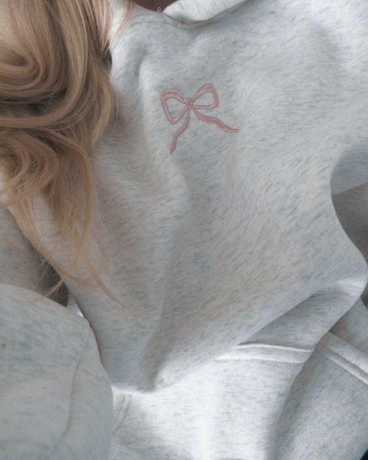 Comfortable women's Elodie hoodie in white, featuring a delicate pink bow. Ideal for feminine loungewear.