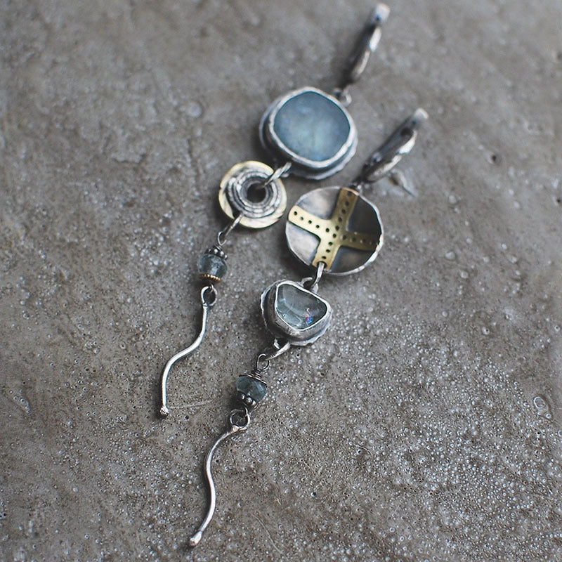 Close-up of women's blue gemstone cross dangle earrings, featuring vibrant blue stones and a delicate design.