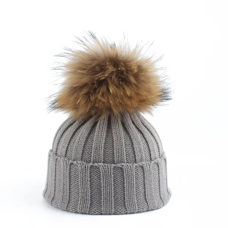 Stylish women's grey knitted winter beanie with a fluffy faux fur pom-pom, a warm and fashionable accessory